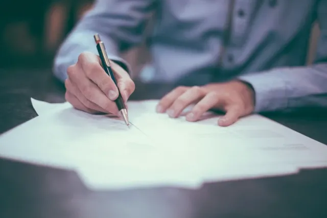 Pessoa assinando um documento sobre a mesa
